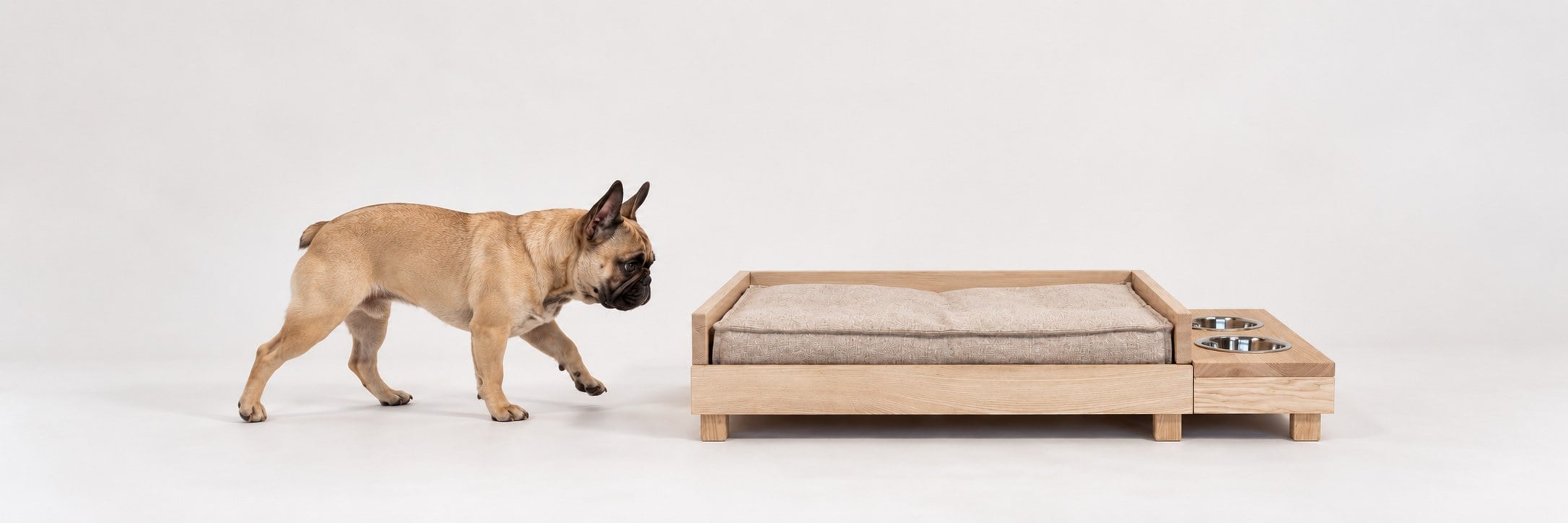A French bulldog walking towards the wooden Trixie dog bed with a mattress and a bowl module